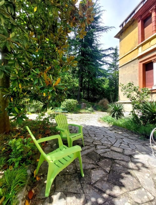 Chaises Adirondack vert vif sur patio en pierre entouré de verdure luxuriante au Palazzo Losio en Piémont, Italie