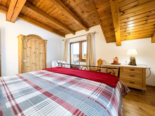 Spacious bedroom in Belvedere Solferino apartment, Auronzo di Cadore, with wooden beamed ceiling, plaid bedding, and mountain