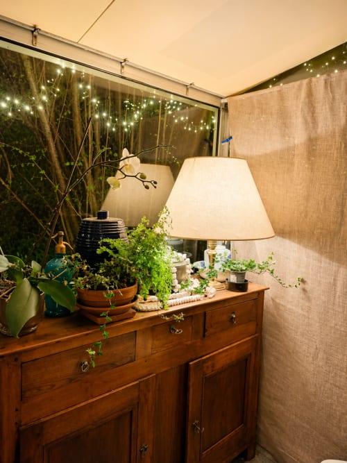 Cozy tent interior at La Villa Malzy with wooden dresser, potted plants, table lamp, and twinkling lights overhead