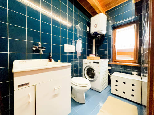 Modern bathroom in Belvedere Solferino apartment with blue tile walls, white sink vanity, toilet, washing machine, and wooden