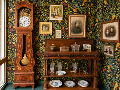 Vintage room display at La Villa Malzy with ornate wooden clock, floral wallpaper, portraits, and antique furniture in