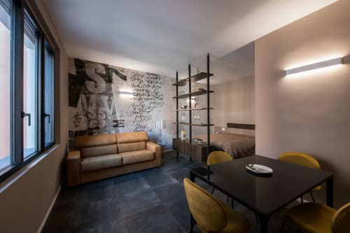 Appartamento Sibilla a Parma con divano in pelle marrone, tavolo da pranzo nero con sedie gialle, opere d'arte e libreria