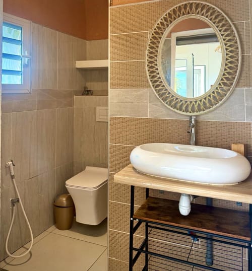 Salle de bain moderne du studio Kaz Kafe à Mamoudzou, avec lavabo ovale, miroir décoratif et douche