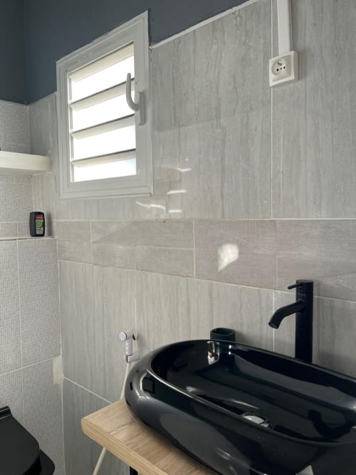 Modern bathroom with black vessel sink, black faucet, and large mirror window in Kaz Kafe Studio Océan, Mayotte