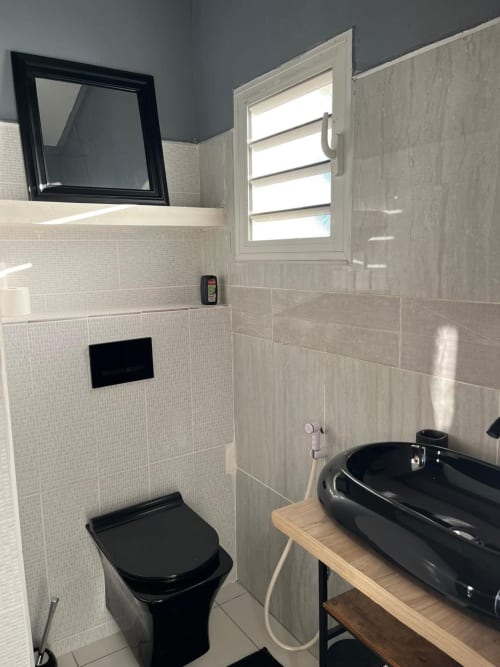 Modern bathroom at Kaz Kafe studio with black toilet, pedestal sink, white tile walls, and window at the sea view apartment