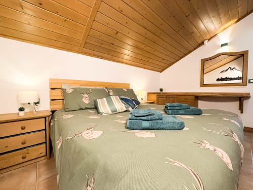 Accogliente camera da letto in montagna con soffitto in legno, biancheria in tonalità salvia e arredamento alpino a Sappada