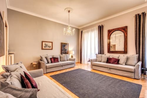 Elegante soggiorno nell'appartamento Downtown Srl a Roma con tre divani beige, lampadario di cristallo, pavimenti in legno e bordeaux