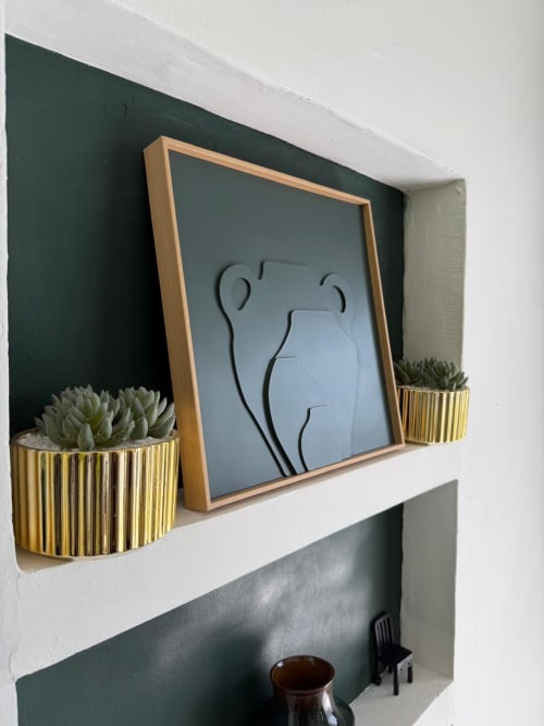 Studio Continent wall decor with framed art, succulents in gold planters, and dark green accent wall at Kaz Kafe
