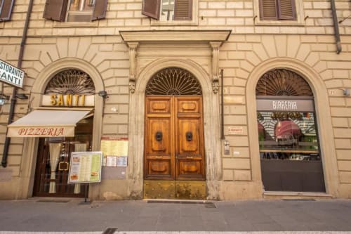 Facciata storica in pietra a Roma con finestre ad arco, portoni in legno, pizzeria e birreria nel centro città