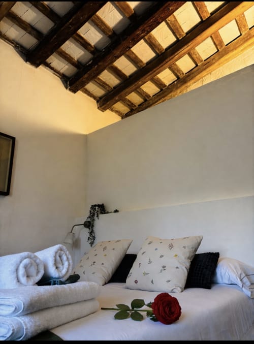 Cozy bedroom at Mas Ribas Hotel, Palamós with exposed wooden beams, white walls, decorative pillows, rolled towels, and red