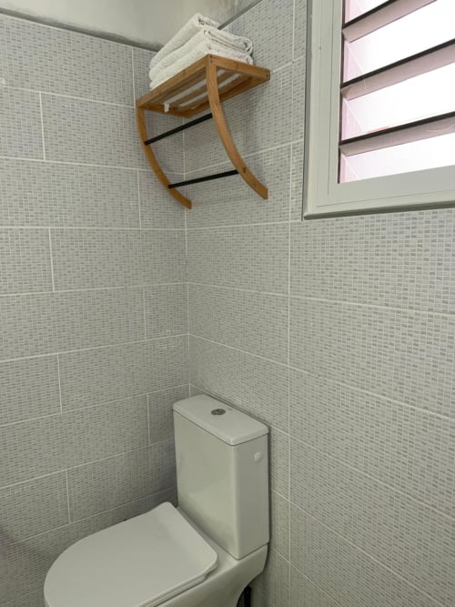 Modern bathroom at Kaz Kafe studio with white tile walls, toilet, and wooden towel rack in Mamoudzou