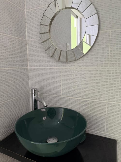 Modern bathroom sink with green bowl vessel, chrome faucet, and decorative sunburst mirror at Kaz Kafe studio apartment in