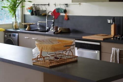 Cuisine moderne du gîte Kaz Kafe à Mamoudzou avec plans de travail noirs, panier en osier et vue sur le jardin