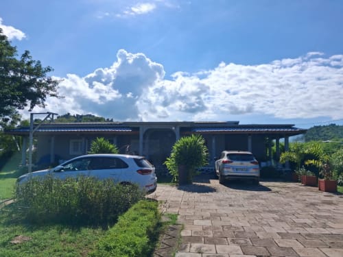 Gîte Kaz Kafe à Mamoudzou avec allée, deux voitures garées, vue sur jardin et ciel bleu