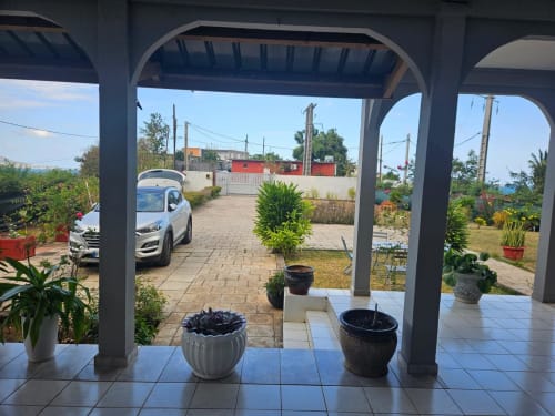 Terrasse couverte du cottage Kaz Kafe avec vue sur le jardin, plantes en pots et allée à Mamoudzou