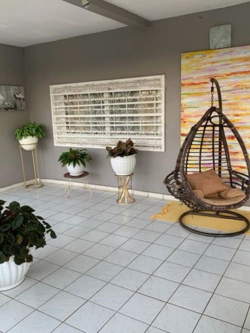Intérieur lumineux du Kaz Kafe avec chaise suspendue, plantes en pot, carrelage blanc et œuvres colorées à Mamoudzou