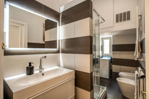 Bagno moderno nell'appartamento Diocleziano Triple, Roma. Doppio lavabo, rivestimento in piastrelle a righe, box doccia in vetro, bidet e