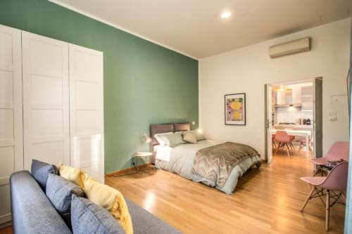 Monolocale moderno a Roma con parete verde, letto matrimoniale, pavimenti in legno, angolo cottura e zona soggiorno