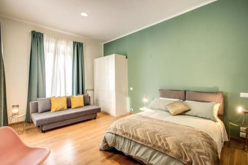 Ampia camera da letto in appartamento romano con parete accent verde, letto matrimoniale, divano e pavimenti in legno - Triple room Diocleziano