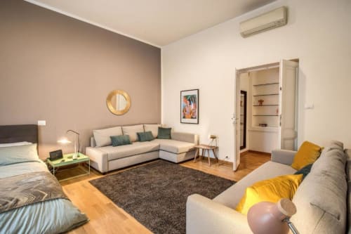 Monolocale moderno a Roma con divano beige, letti gemelli, pavimenti in legno e arredi contemporanei