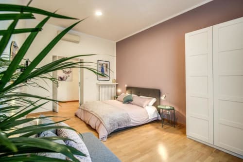 Ampia camera da letto in appartamento nel centro di Roma con letto matrimoniale, parete accent rosa, pavimento in parquet e piante verdi
