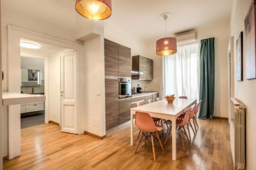 Cucina e zona pranzo di moderno appartamento romano con pavimenti in legno, sedie arancioni e angolo cottura attrezzato