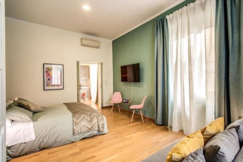 Spaziosa camera da letto a Roma con parete d'accento verde, pavimenti in legno, TV, sedie rosa e luce naturale dalle ampie finestre