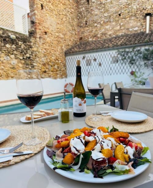 Outdoor poolside dining at Casa Sibarita with salad, wine, and stone courtyard in Rafelguaraf