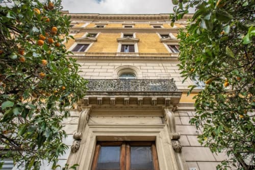 Facciata storica di edificio romano con piani superiori in ocra gialla e ingresso in pietra ornato, circondato da rigoglioso edera verde con accenti arancioni