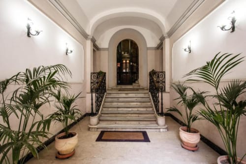 Elegante corridoio di appartamento romano con soffitto a volta, piante in vaso e maestosa scala ornamentale all'ingresso