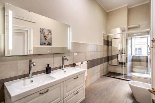 Bagno moderno in appartamento romano con doppio lavabo, doccia aperta e piastrelle in toni neutri