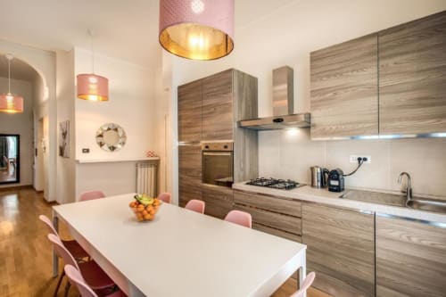 Moderna zona cucina-pranzo in appartamento romano con mobili in legno, lampadari rosa e tavolo da pranzo
