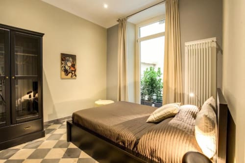 Camera da letto moderna in appartamento romano con letto matrimoniale, armadio nero, ampie finestre, tende beige e balcone con vista sulla città