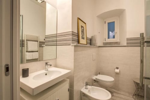 Bagno moderno con lavandino bianco, bidet, toilet, portasciugamani a righe e dettagli in piastrelle nell'appartamento Cavour Cinque Terre, Roma