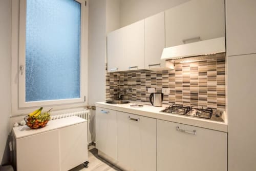 Cucina moderna in appartamento Downtown Srl Roma con ante bianche, rivestimento a piastrelle righe, fornello a gas e finestra con vista città