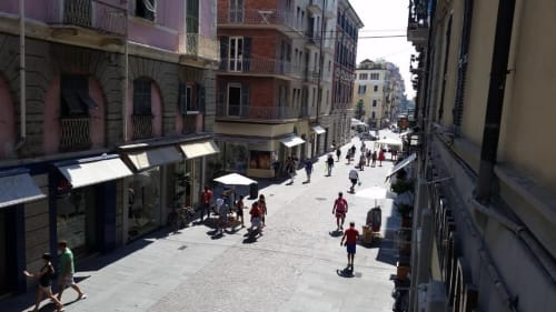 Vivace scena di strada romana con edifici storici colorati, negozi e passanti che godono della soleggiata piazza cittadina
