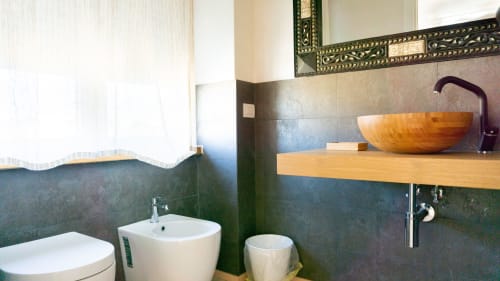 Modern bathroom with dark tile walls, wooden sink countertop, and designer wooden basin at Versilia Panoramic Luxury hotel in