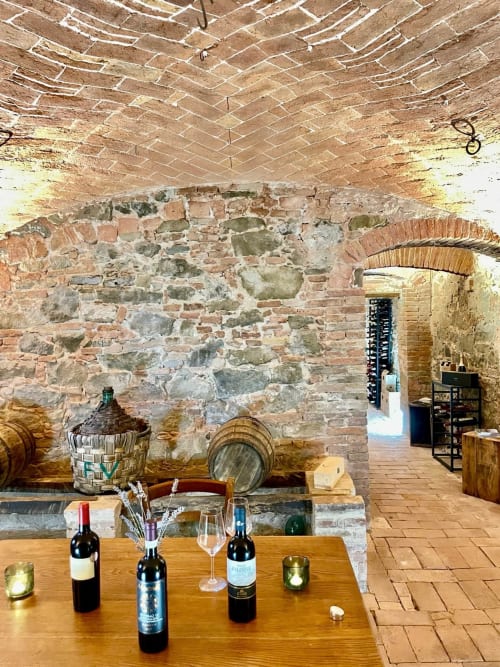 Historic wine cellar at Agriturismo CasaViva with stone walls, wooden table, wine bottles, and rustic barrels