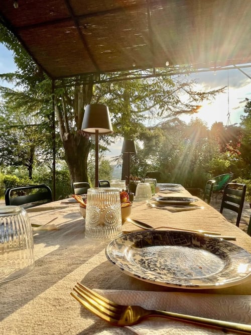 Elegant outdoor dining setup at Agriturismo CasaViva with sunset views, ivy-covered pergola, and countryside landscape.