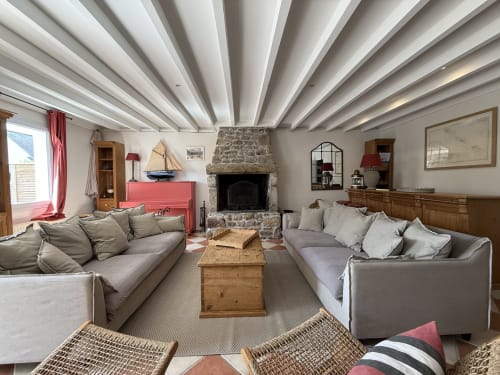 Salon spacieux de la villa ATICA à Soleilmeretsable, Hoëdic, avec cheminée en pierre, canapés gris et plafond à poutres