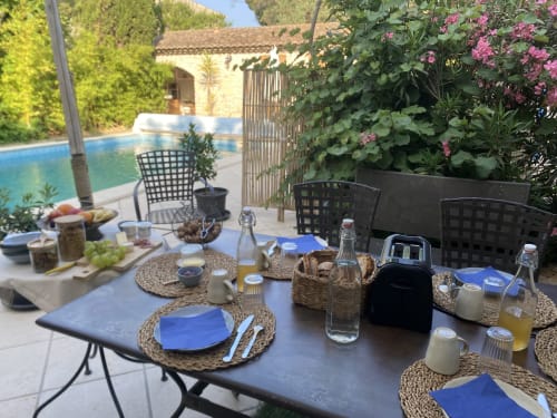 Espace de restauration extérieure au gîte Le Patio aux Oiseaux à La Ciotat avec table bleue, piscine et fleurs roses