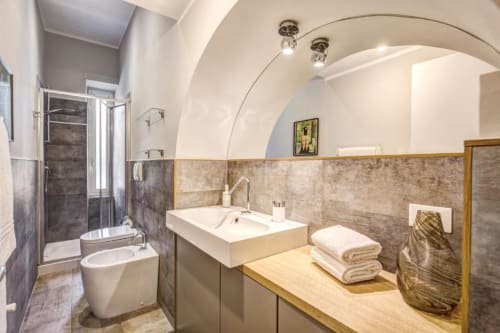 Modern bathroom in Cinque Terre Stylish apartment, Roma with arched ceiling, dark tile walls, white sink, toilet, and wooden