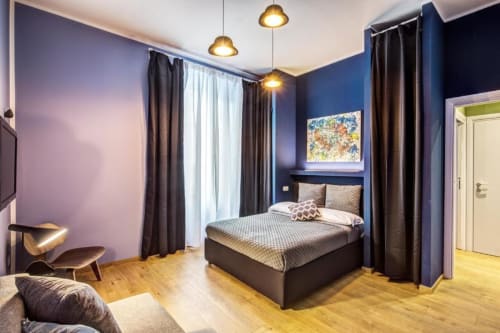 Modern bedroom in Rome apartment with blue walls, wooden floors, pendant lights, and contemporary furnishings
