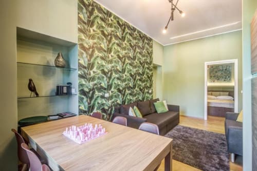 Stylish Rome apartment living area with botanical wallpaper, wooden dining table, brown sofa, and open bedroom door
