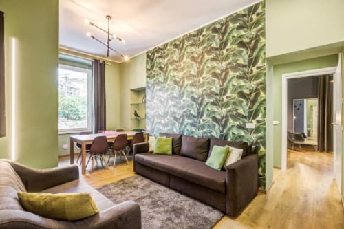 Modern Rome apartment living room with green accent wall, botanical wallpaper, dark sofa, natural wood floors, and