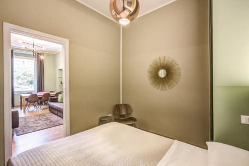 Cinque Terre Stylish bedroom in Rome with bed, sunburst mirror, pendant light, and open view to living area