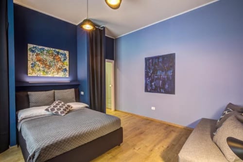 Modern bedroom in Rome apartment with blue walls, queen bed, wooden floors, and contemporary art