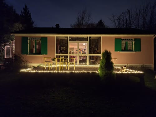 La Villa Malzy in Vétheuil glows warmly at night, featuring a modern cottage with green shutters, yellow café seating, and