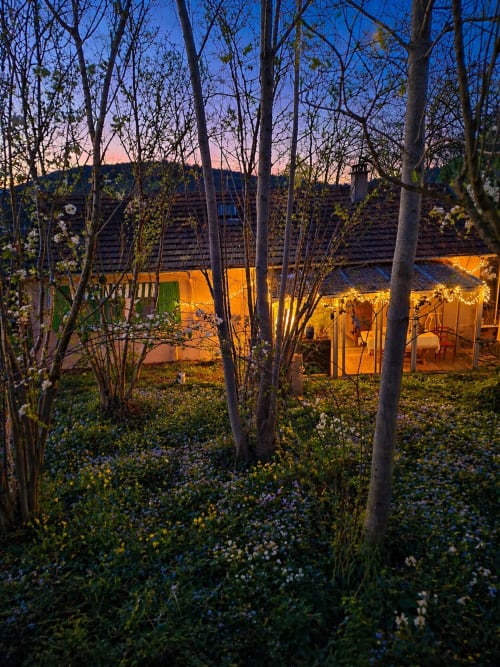 Illuminated luxury glamping tent at La Villa Malzy in Vétheuil, France, surrounded by wildflowers and birch trees at dusk