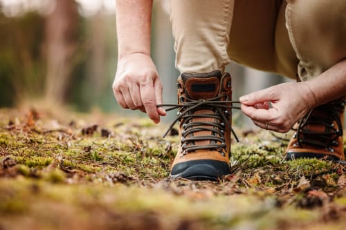 Hiker tying brown hiking boots on forest ground near Casa Sibarita, Rafelguaraf